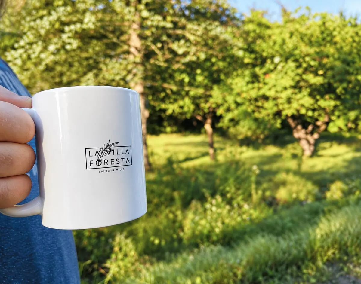 Une main qui tient une tasse La Villa Foresta devant un verger bien vert