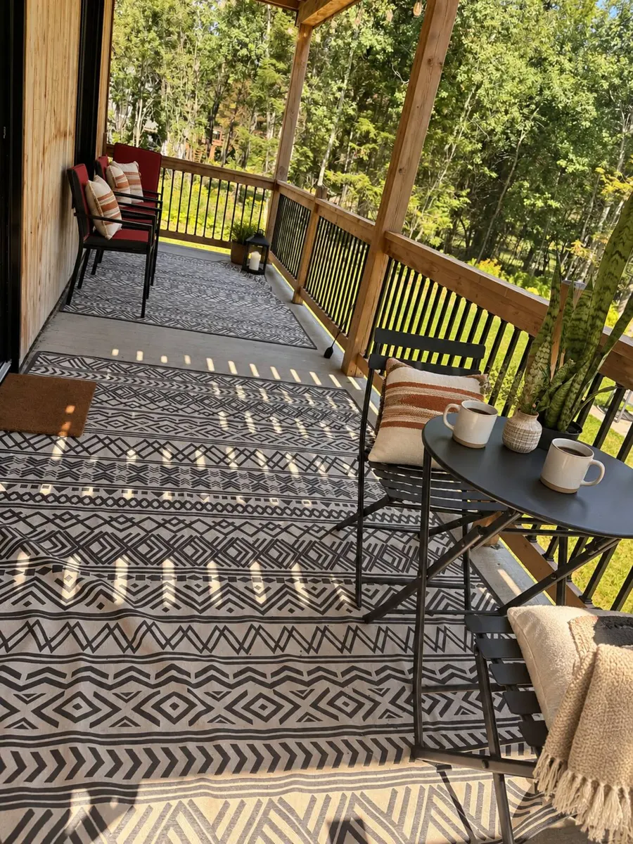 The covered deck with a patterned outdoor rug, a bistro table and two coffee cups