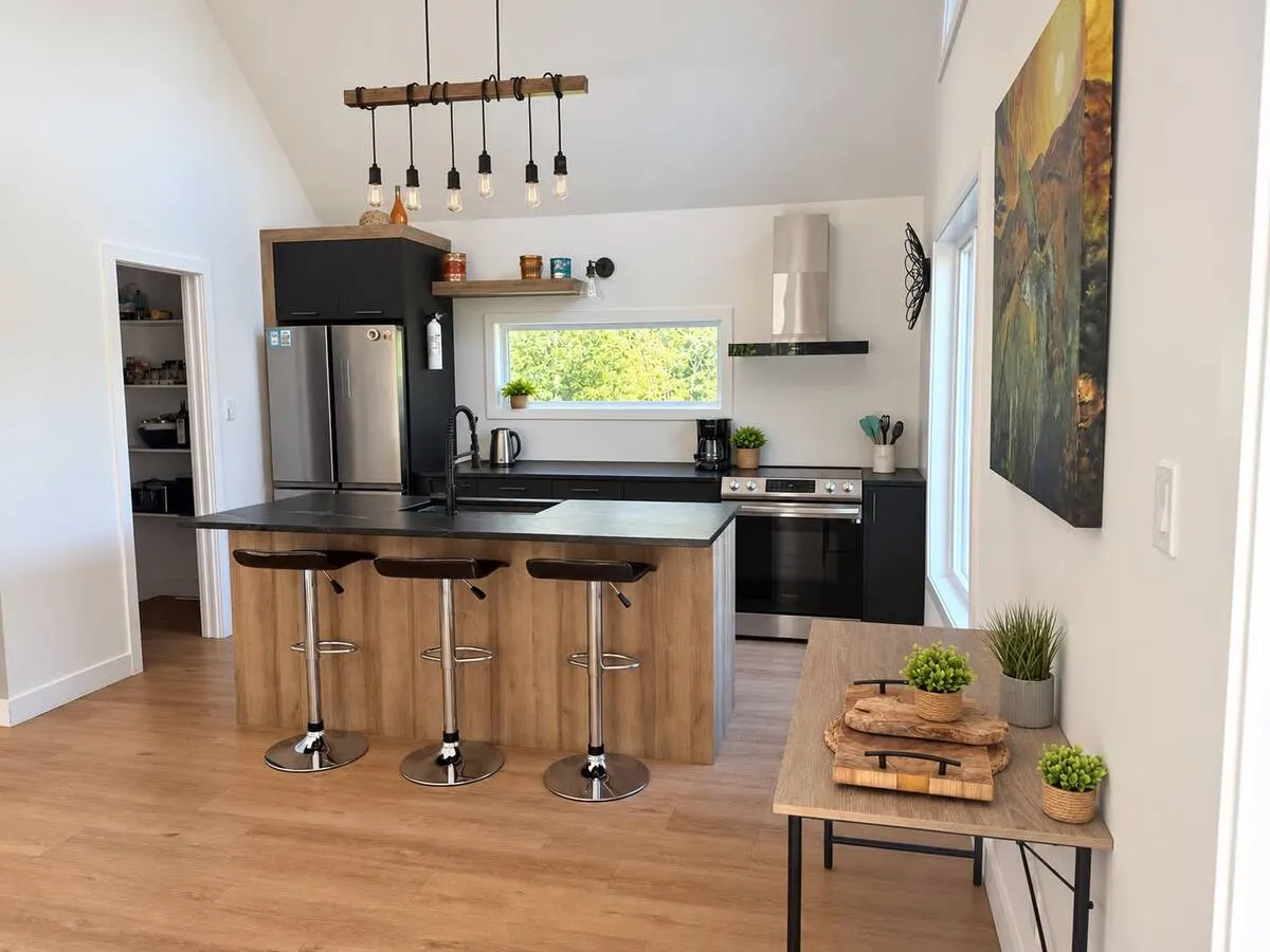 A modern kitchen with a wooden island, three bar stools and black cabinets