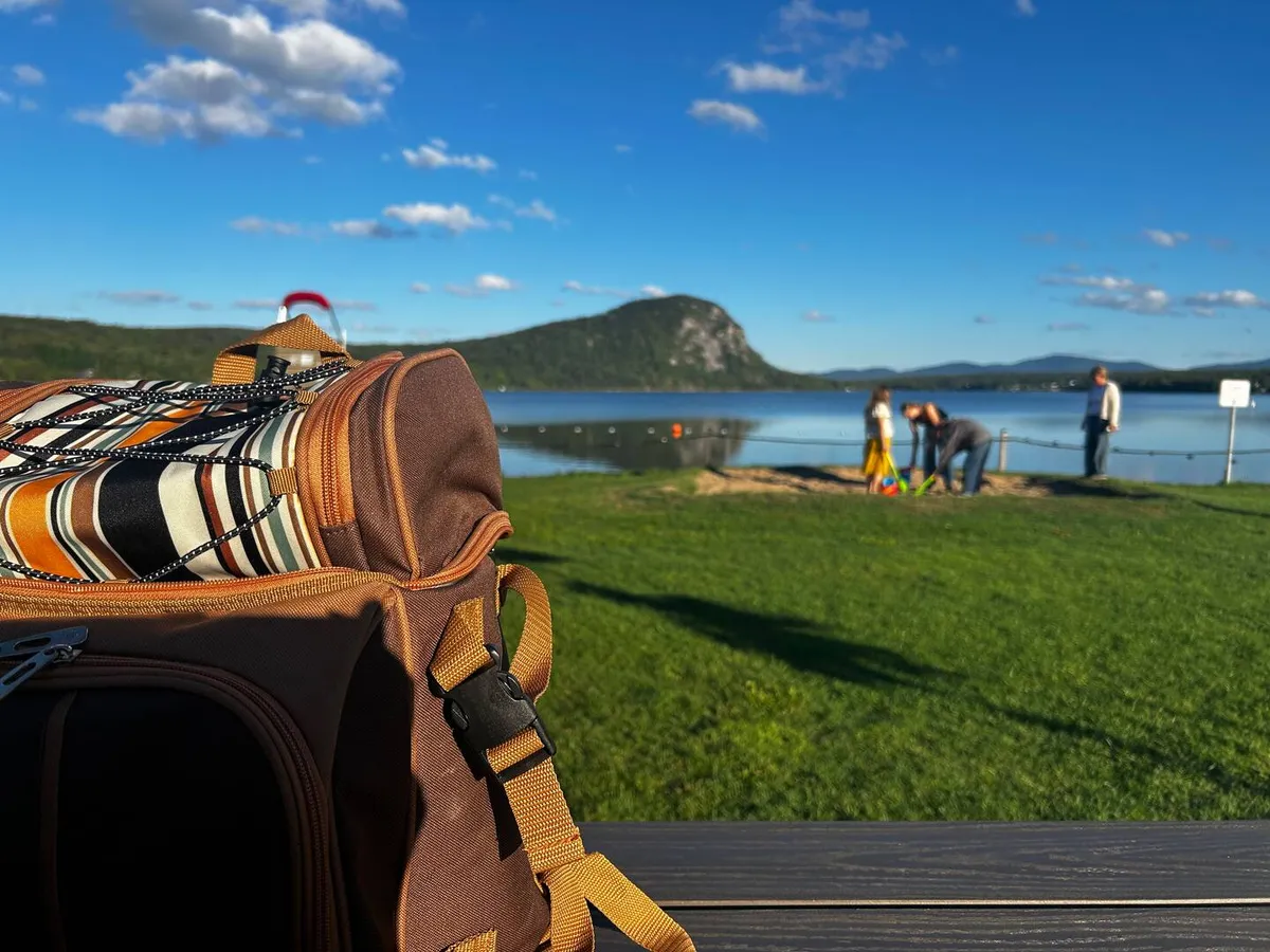 A picnic backpack on the grass at Lac Lyster, the cliff of Mont Pinacle across the water